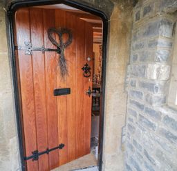 A wooden front door partially open with black metal hinges and a heart-shaped wreath at Bear's Cottage in Bretforton near Broadway