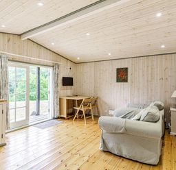 A room with two armchairs a small table and chairs a wall mounted television and sliding glass doors at Lakeside Cabin in Sheldon Blackdown Hills
