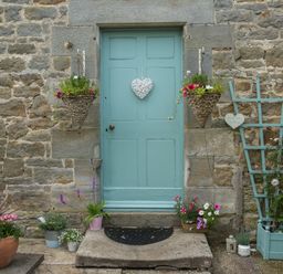 A stone wall with a blue door decorated with hanging baskets and potted plants at West Wing Cottage in Hexham