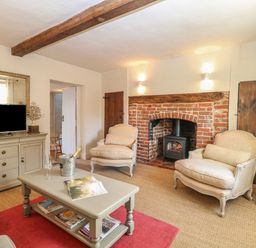 A living room with two armchairs a coffee table and a television near a brick fireplace at Bridge Cottage in Aylsham
