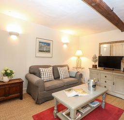 A living room with a gray sofa a coffee table and a TV cabinet at Bridge Cottage in Aylsham