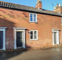 A brick exterior of a row of cottages with dark doors and white window frames at Bridge Cottage in Aylsham