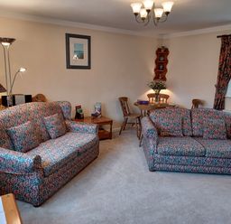 A living room with two patterned sofas a wooden dining table with chairs and a lamp at Magpie Cottage in South Brewham