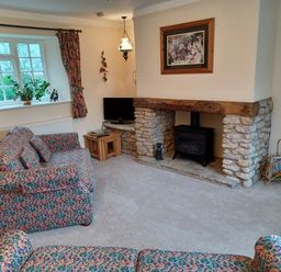 A sitting room with patterned sofas a stone fireplace a window with curtains and a television at Magpie Cottage South Brewham