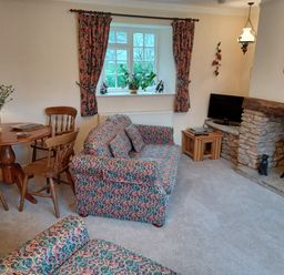 A living room with patterned sofas a wooden dining table with chairs and a stone fireplace at Magpie Cottage South Brewham