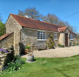 A stone cottage with a red tiled roof and potted plants on a gravel path in a grassy yard at Magpie Cottage in South Brewham