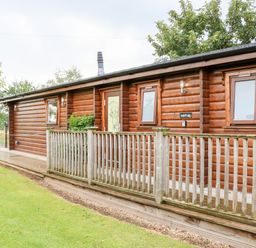 A wooden log cabin with a wooden railing and green lawn at Heathcliff in Northallerton