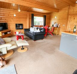 An open living room with a black sofa beige recliner red dining chairs and a television at Heathcliff in Northallerton