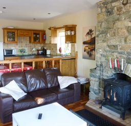 A living area with a brown leather sofa a white table a stone fireplace and a wooden kitchen at Ti Sheamuis in Cashel near Carna County Galway