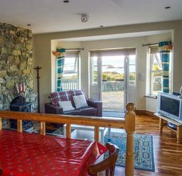 A living room with a stone fireplace a sofa and a television near windows and doors at Ti Sheamuis in Cashel near Carna County Galway