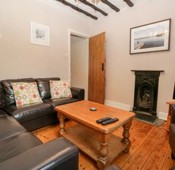 A living room with black leather sofas and colorful cushions a wooden coffee table a small black fireplace a wooden door and a television at Fishers Retreat in Bowness-On-Windermere