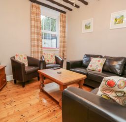 A living room with leather sofas and armchairs around a wooden coffee table and a television on a wooden stand at Fishers Retreat in Bowness-On-Windermere