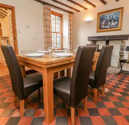 A dining room with a wooden table and four chairs set with plates and glasses at Fisher's Retreat in Bowness-On-Windermere