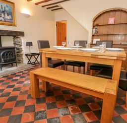 A dining room with a wooden table, bench, chairs, a stove in a stone fireplace, and a wooden cabinet at Fishers Retreat in Bowness-On-Windermere