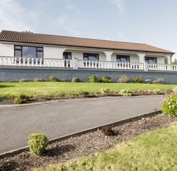 A single story house with a tiled roof a white balustrade in front and a garden with grass and bushes at Aras Iosgan in Carraroe County Galway