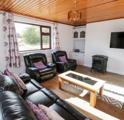 A living room with black leather sofas a wooden coffee table a wood stove and a wall-mounted tv at Aras Iosgan in Carraroe County Galway