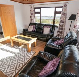 A living room with black leather sofas a wooden coffee table patterned rug and floral curtains at Aras Iosgan Carraroe County Galway