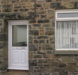 A white door and a window with lace curtains set in a stone wall of a building at Rowan Cottage in Builth Wells