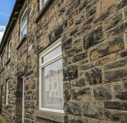 Stone exterior wall of a house with two windows and wires on the wall on a street
