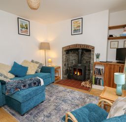 A living room with a blue sofa and armchair a wood burning stove and wooden shelves at Rowan Cottage in Builth Wells
