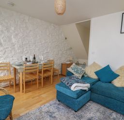 A dining area with wooden chairs and table next to a blue sofa with cushions in a living room at Rowan Cottage in Builth Wells