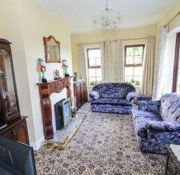 A living room with two floral patterned sofas a fireplace wooden cabinets and windows with curtains at Belladrihid Cottage Ballysadare near Sligo County Sligo