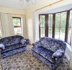 A room with two floral patterned sofas near windows with curtains and a patterned carpet at Belladrihid Cottage Ballysadare near Sligo County Sligo