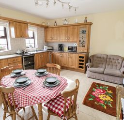 A kitchen with wooden cabinets a round dining table with red and white tablecloth and sofa at Belladrihid Cottage Ballysadare near Sligo County Sligo