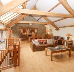 A living area with exposed wooden beams leather sofas wooden coffee table and dining table in a barn conversion at Cowslip Barn in Cornworthy near Dittisham