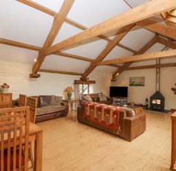 A living room with exposed wooden beams wooden dining chairs sofas a fireplace and a television at Cowslip Barn Cornworthy near Dittisham