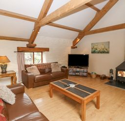 A living room with wooden beams a fireplace two brown leather sofas a wooden coffee table and a television at Cowslip Barn in Cornworthy near Dittisham