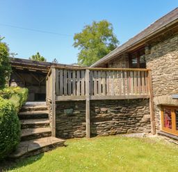 An outdoor area with stone steps leading to a wooden deck beside a stone building with windows at Cowslip Barn in Cornworthy near Dittisham