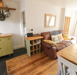 A living room with a brown sofa, wooden dining table, green cabinet, pots hanging on wall, and wooden floor at Snowdon View Llanberis