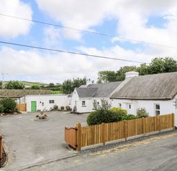 A traditional white house with a thatched roof and wooden fence surrounding a concrete driveway at Whispering Willows - The Thatch in Carndonagh County Donegal