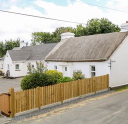 A white house with a thatched roof and a wooden fence in the front at Whispering Willows - The Thatch in Carndonagh County Donegal
