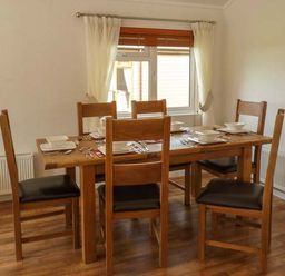 A dining room with a wooden table set for six and wooden chairs at Morgan Lodge in Hewish near Weston-super-Mare