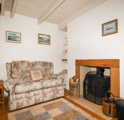 A living room with a floral sofa next to a wooden fireplace and side table at The Ark Cottage in St Blazey
