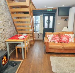 A living room with a wood stove wooden staircase dining table and brown leather sofa at Stable Cottage in Pembroke