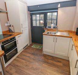 A kitchen with white cabinets wooden countertops a black oven a sink and a black door at Stable Cottage in Pembroke