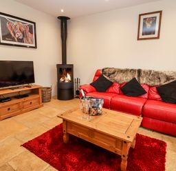 A living room with a red leather sofa wooden coffee table and a television at Cow Byre in Great Tew near Chipping Norton