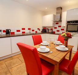 A kitchen with white cabinets red and white tiled backsplash wooden table set with dishes and red chairs at Cow Byre Great Tew near Chipping Norton