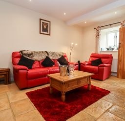 A living room with red leather sofa and armchair wooden coffee table and red rug at Cow Byre in Great Tew near Chipping Norton