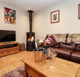 A living room with a wood burning stove leather sofa and wooden coffee table at The Stables in Great Tew near Chipping Norton
