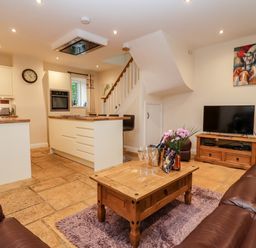 An open plan living room and kitchen with leather sofas wooden coffee table and TV at The Stables Great Tew near Chipping Norton