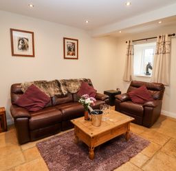 A living room with brown leather sofa and armchair a wooden coffee table with flowers and glasses on a rug at The Stables Great Tew near Chipping Norton