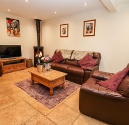 A living room with leather sofas a wooden coffee table a television and a wood burning stove at The Stables in Great Tew near Chipping Norton