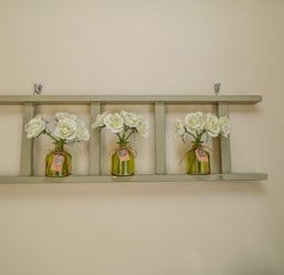 Three small green glass jars with white flowers on a green wooden wall shelf at Ericas eaven Farndale near Kirkbymoorside