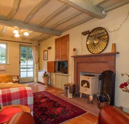 A living room with a fireplace a wood stove a yellow sofa a red patterned rug and a glass door at High House Newton in Cartmel near Cartmel