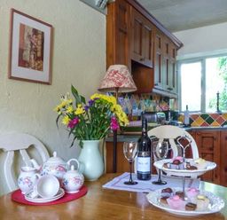 A kitchen with wooden cabinets flowers on a table tea set wine bottle and sweets on High House Newton in Cartmel near Cartmel