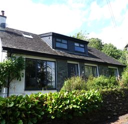 A residential house with a sloped roof and multiple windows surrounded by greenery at Wysteria Cottage in Windermere